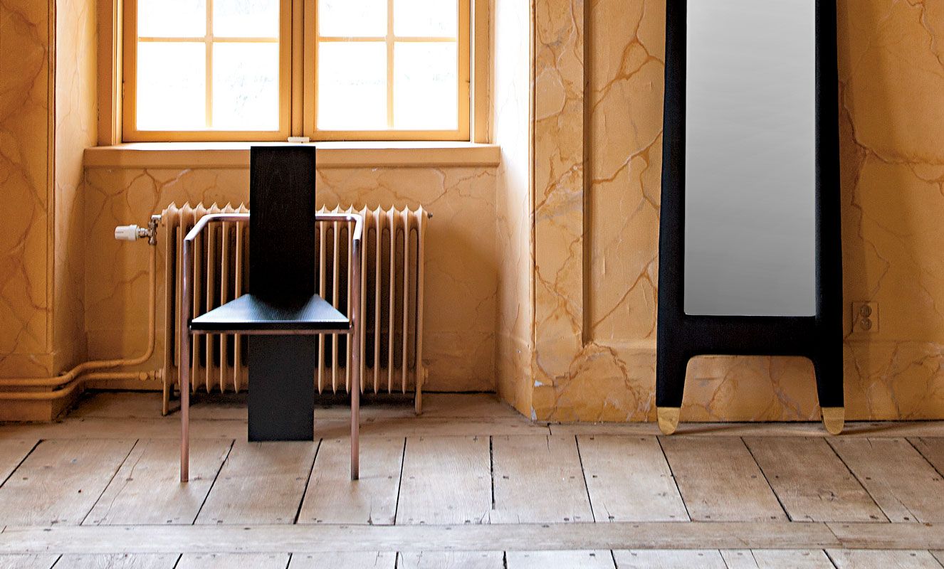 Concrete chair in black and copper in front of a radiator under a window.