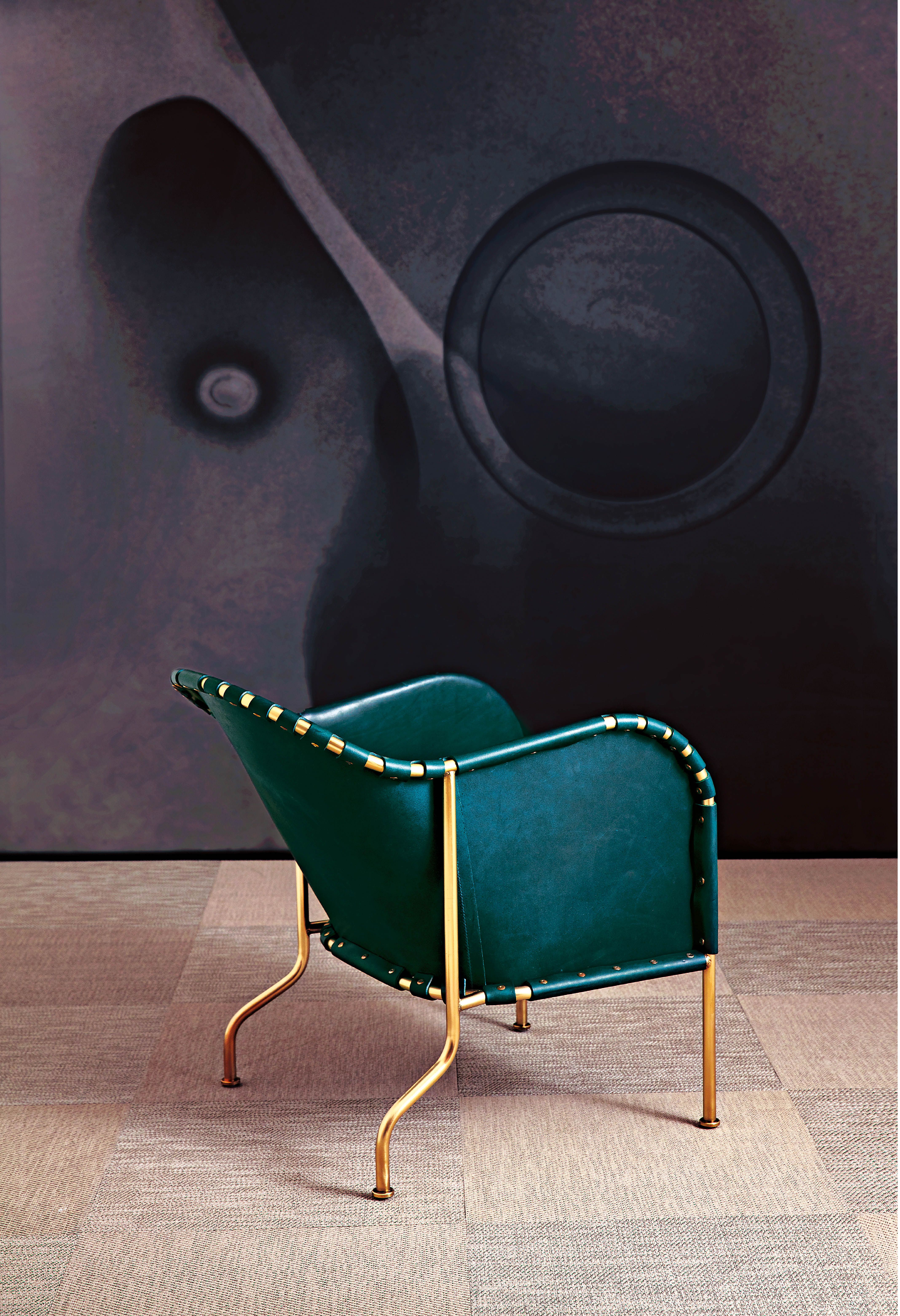A green armchair of the Bruno model with a brass frame on a light carpet.